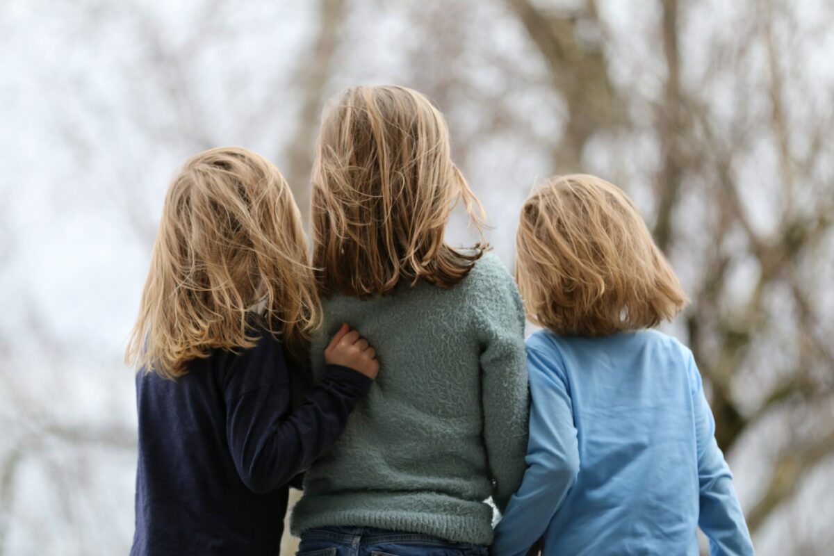 Three children stand closely together, with their backs to the camera